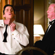 Bruce Wayne attempts to tie his bowtie while Alfred the butler watches on.